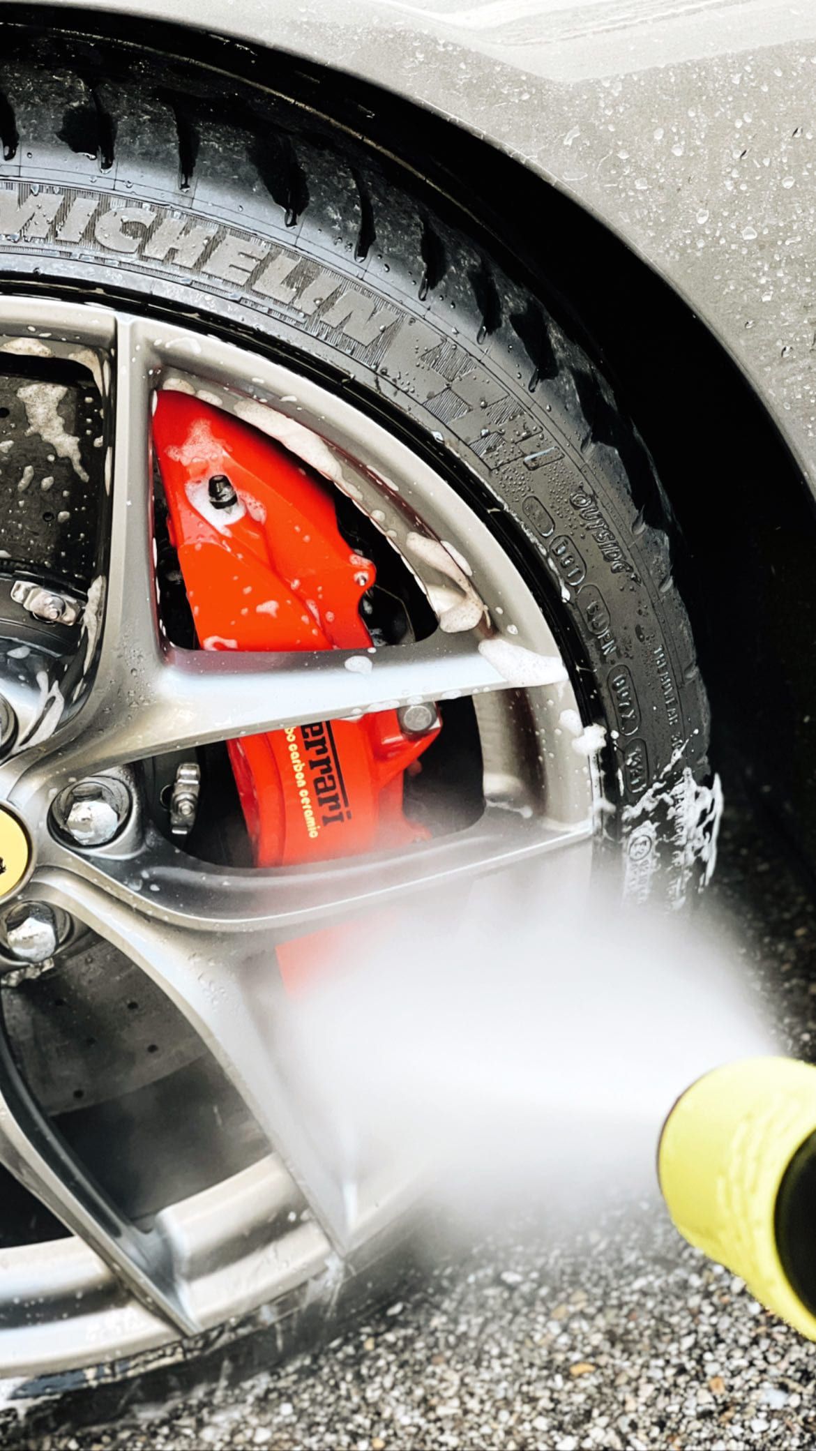 Das Rad eines Ferrari wird mit Schaum und Wasserstrahl gereinigt, der rote Bremssattel trägt den Schriftzug carbon ceramic