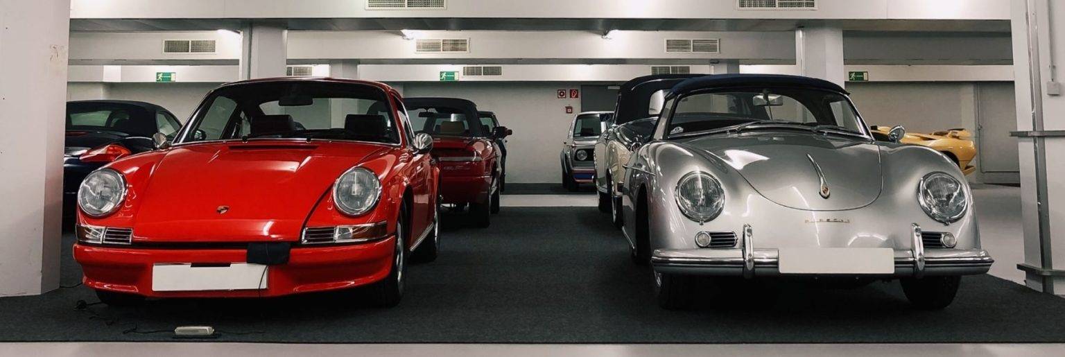Ein roter Porsche 911 und ein silberner Porsche 356 Speedster nebeneinander in der HUBRAUM-Halle, dahinter weitere Klassiker