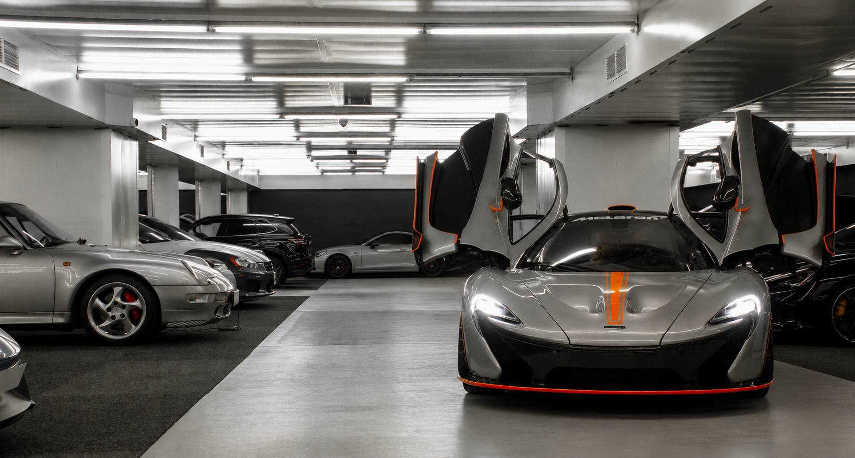 Ein McLaren P1 mit geöffneten Flügeltüren in der HUBRAUM-Halle, links daneben ein Porsche 911 der Baureihe 993, im Hintergrund weitere Sportwagen unter durchgehender Deckenbeleuchtung