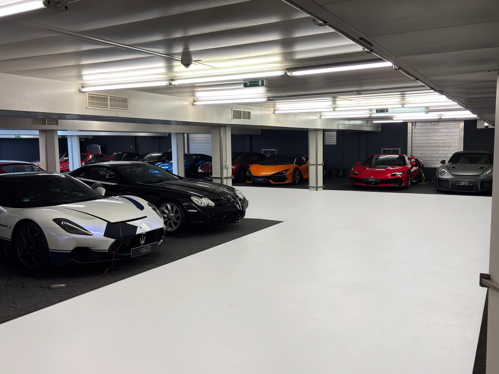 Blick durch die HUBRAUM-Halle: vorn ein weißer Maserati und ein schwarzer Mercedes-Benz SLR, im Hintergrund ein orangefarbener McLaren und ein roter Ferrari