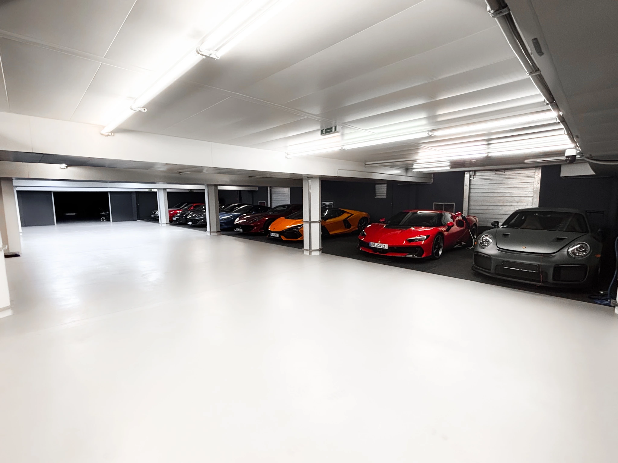 Die freie Fahrfläche der HUBRAUM-Halle mit heller, versiegelter Oberfläche, rechts Stellplätze mit einem roten Ferrari und einem grauen Porsche 911
