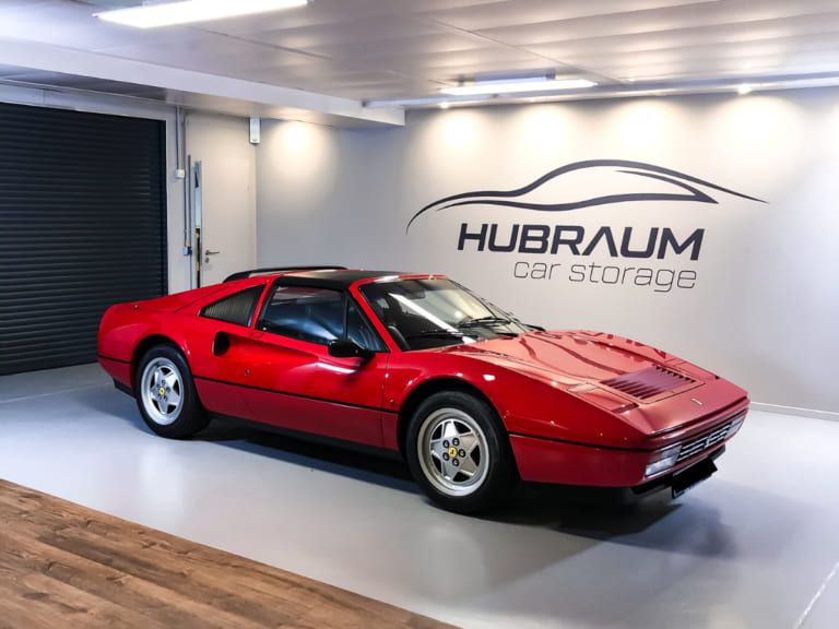 Ein roter Ferrari mit abnehmbarem Dachteil in der HUBRAUM-Halle, dahinter die Wand mit dem Schriftzug HUBRAUM car storage